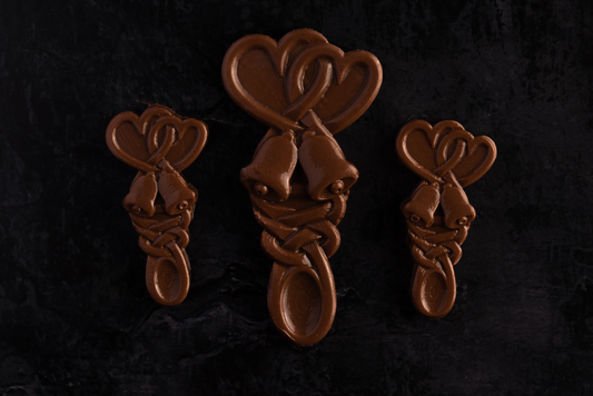 Three handmade Belgian chocolate love spoons with a wedding bells design, displayed on a dark background.