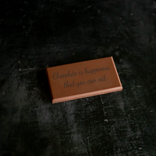 A personalized Belgian milk chocolate bar with text 'Chocolate is happiness that you can eat' printed on it, placed on a dark surface.