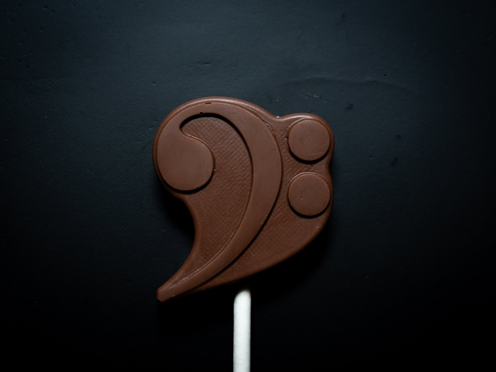 Chocolate lollipop shaped like a musical symbol on a dark background