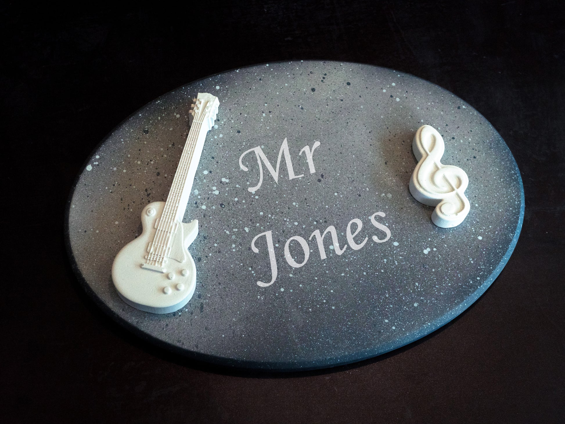 Decorative plaque with 'Mr Jones' engraving, guitar-shaped object, and treble clef on a dark background