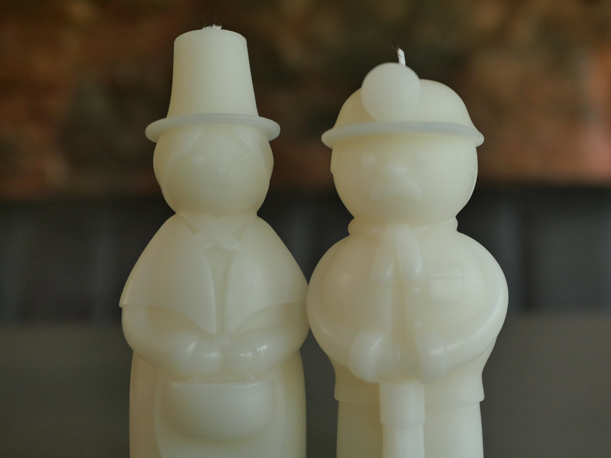 Two white candles shaped like people/ welsh woman, welsh miner with hats on a blurred background