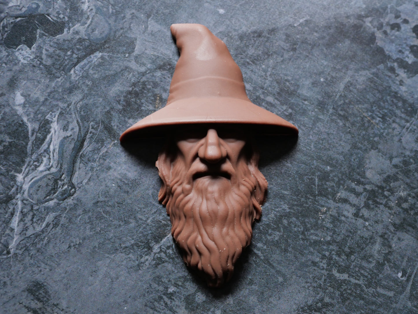 Decorative wizard head with a pointed hat on a textured gray surface