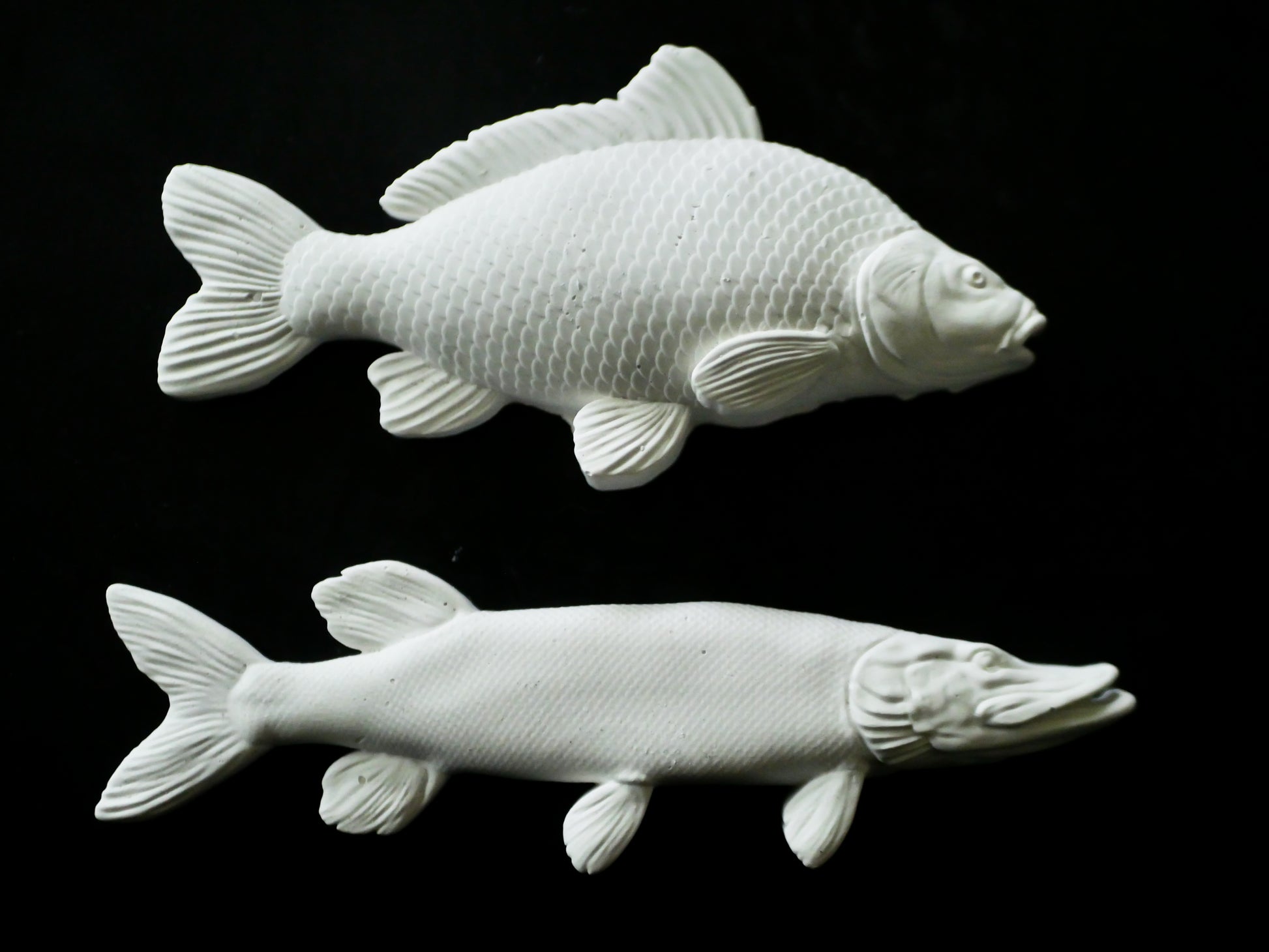 Two white ceramic fish sculptures on a black background
