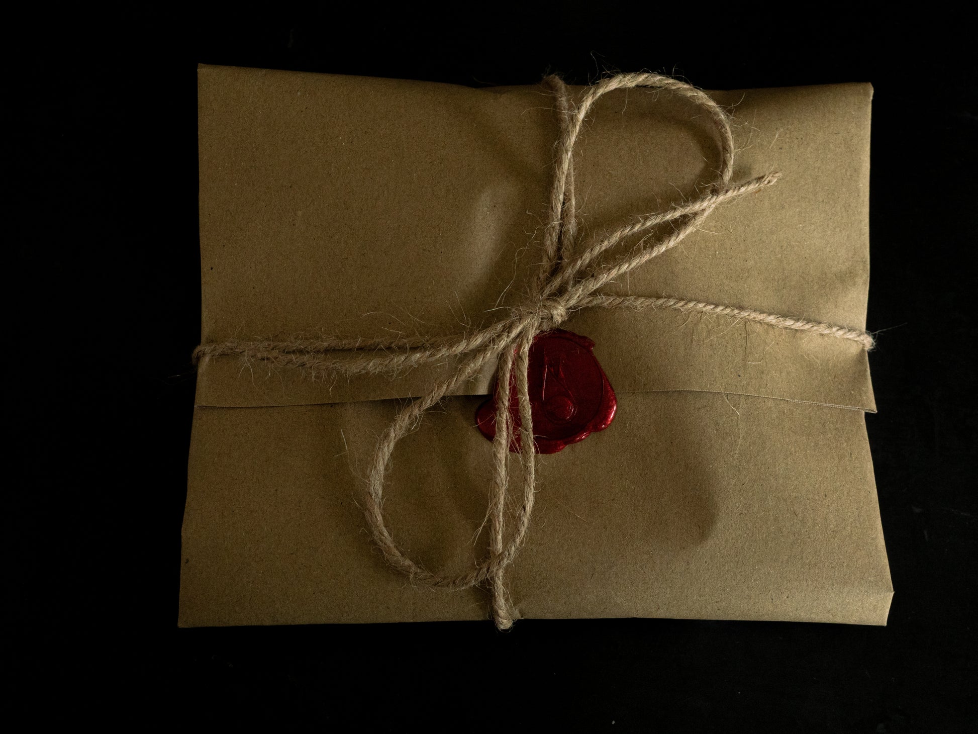 Brown paper parcel gift with string and red wax seal on a black background