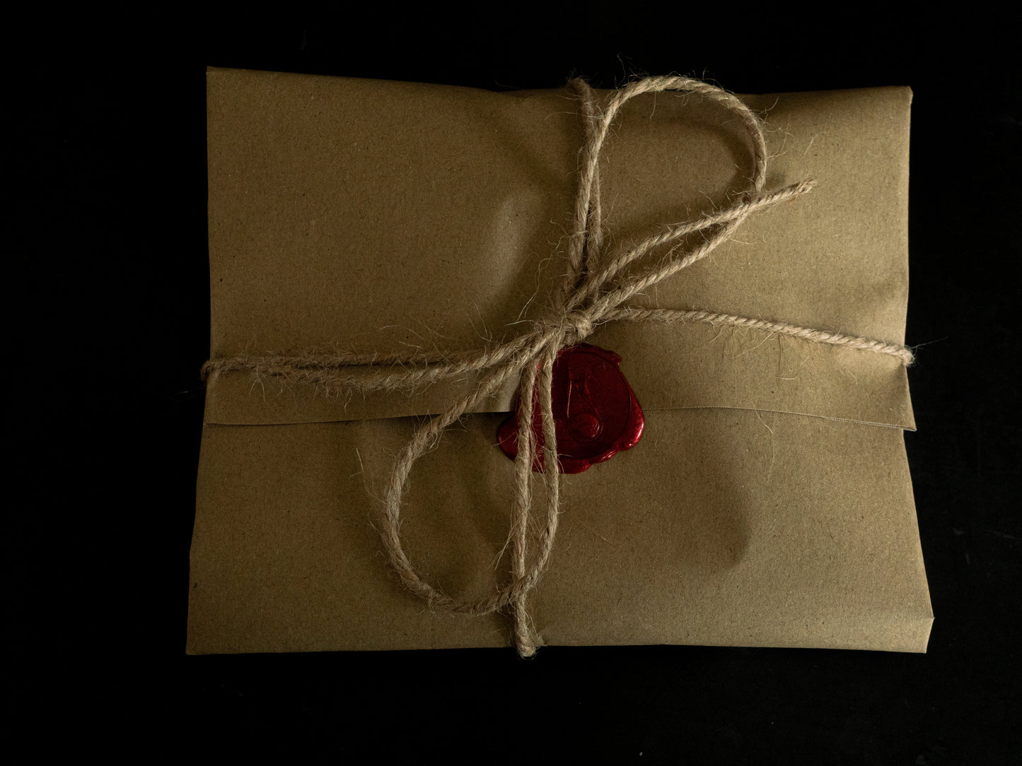 Brown paper parcel gift with string and red wax seal on a black background