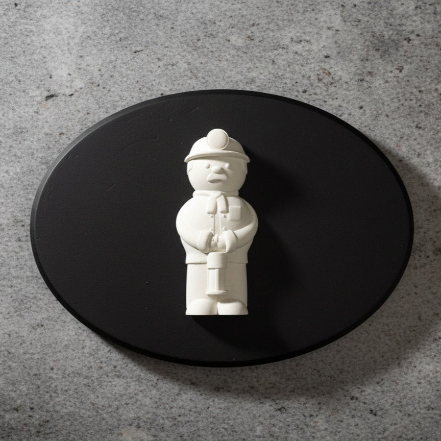 White figurine of welsh miner on a black oval platform against a gray concrete background