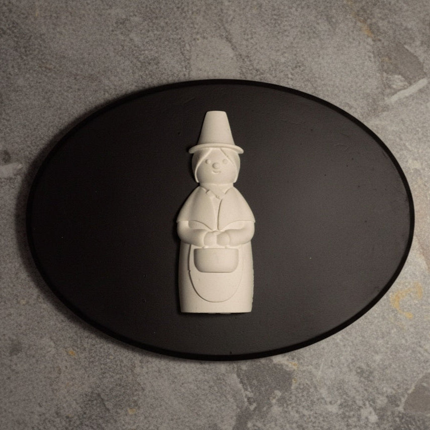 White ceramic welsh lady on a black oval plate against a gray stone background