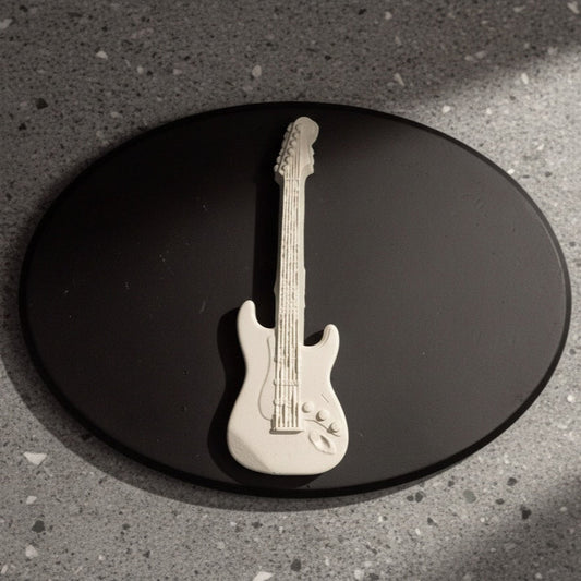 White guitar-shaped object on a black oval plaque with a gray concrete background