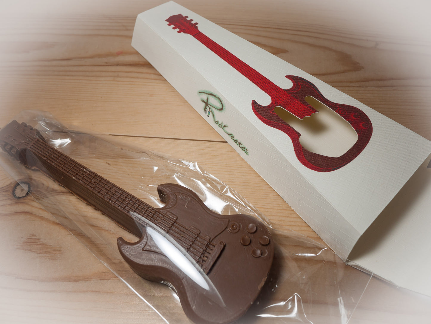 A Gibson SG guitar shaped chocolate wrapped in plastic next to a gift box.