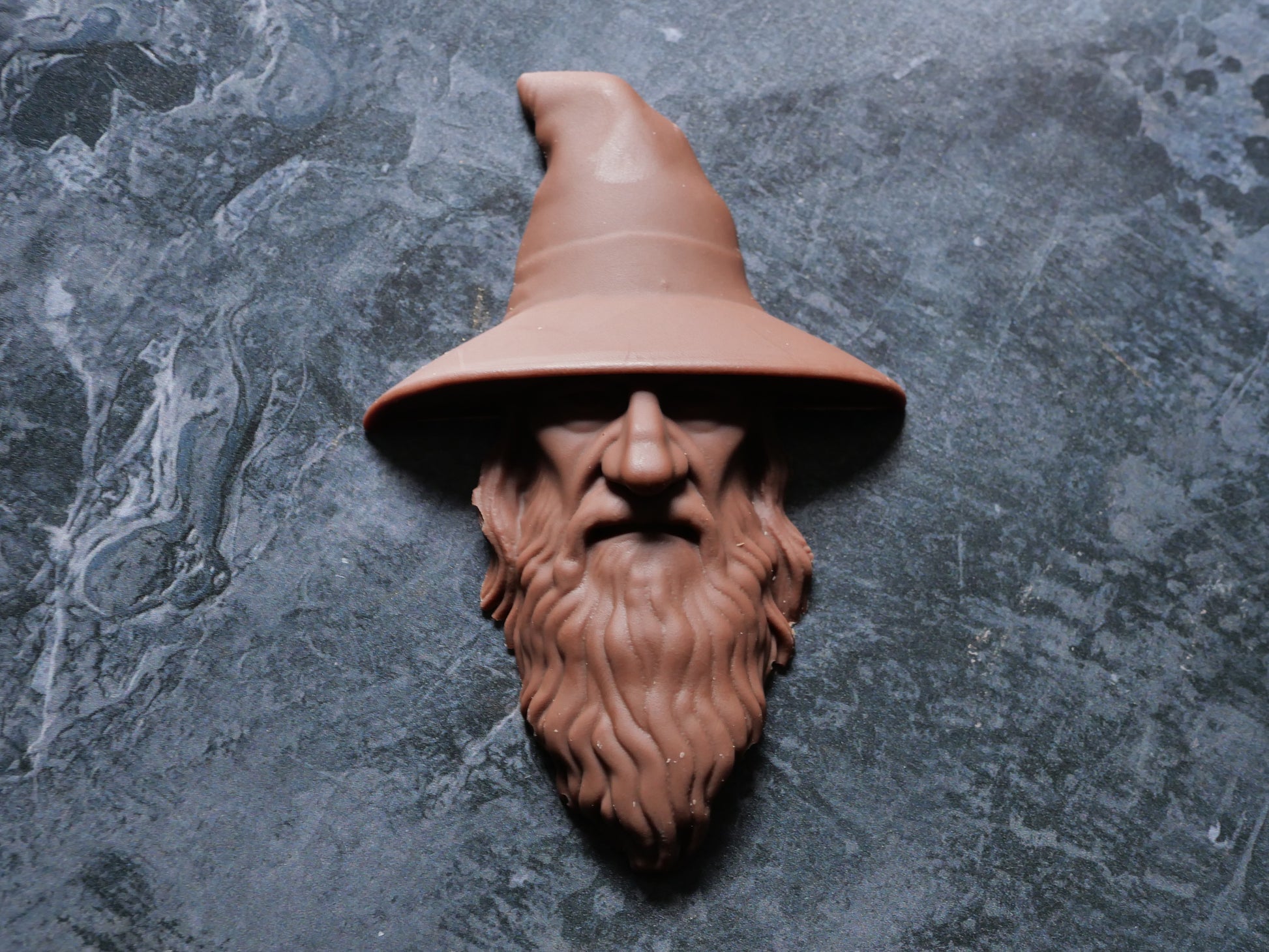 Decorative wizard head with a pointed hat on a textured gray surface