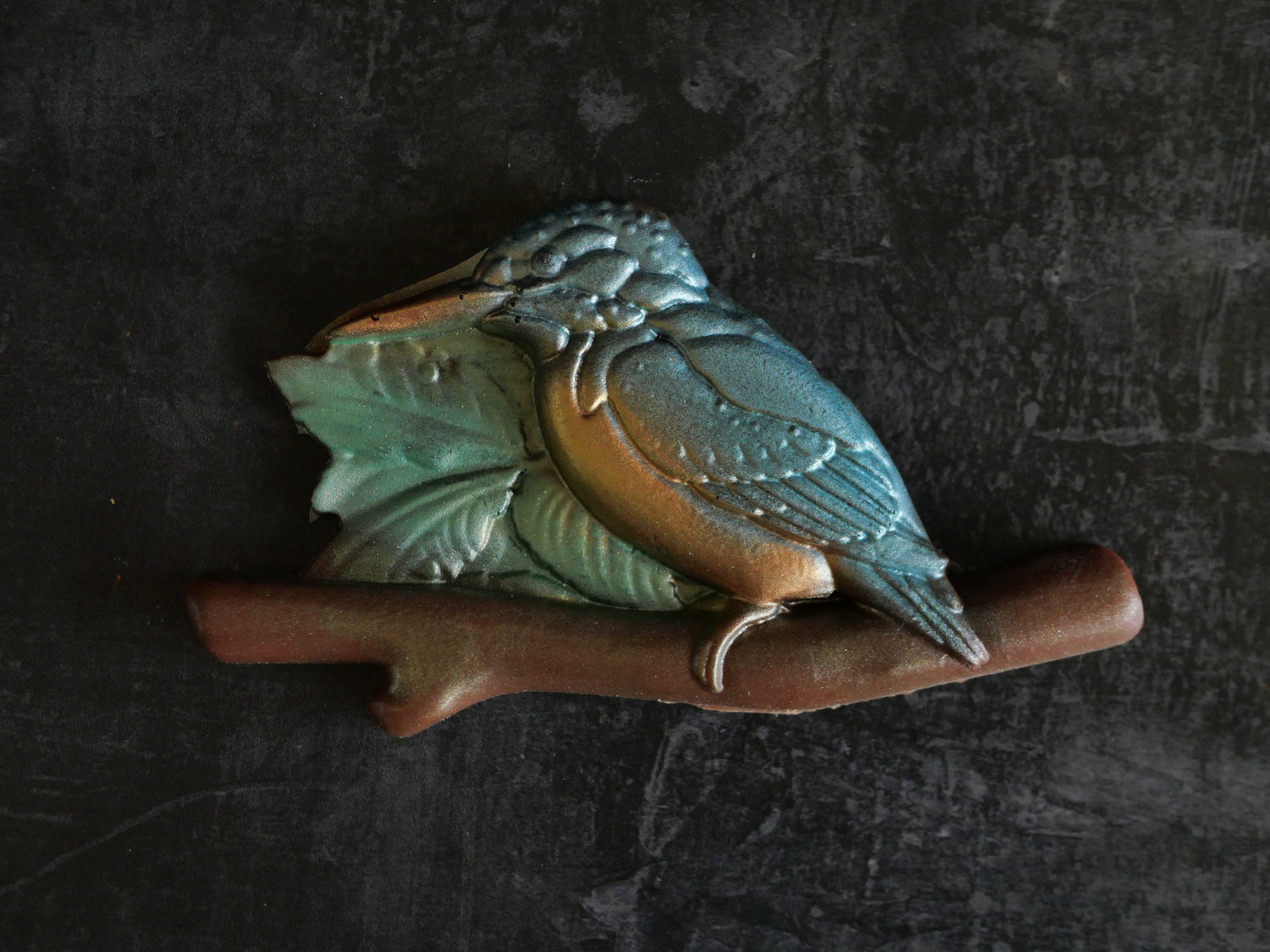 Decorative painted chocolate bird on a branch with leaves against a dark background