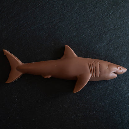 A brown shark-shaped confection, likely a chocolate bar or candy, displayed on a dark textured slate background.