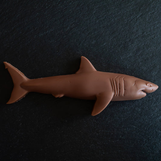 A brown shark-shaped confection, likely a chocolate bar or candy, displayed on a dark textured slate background.